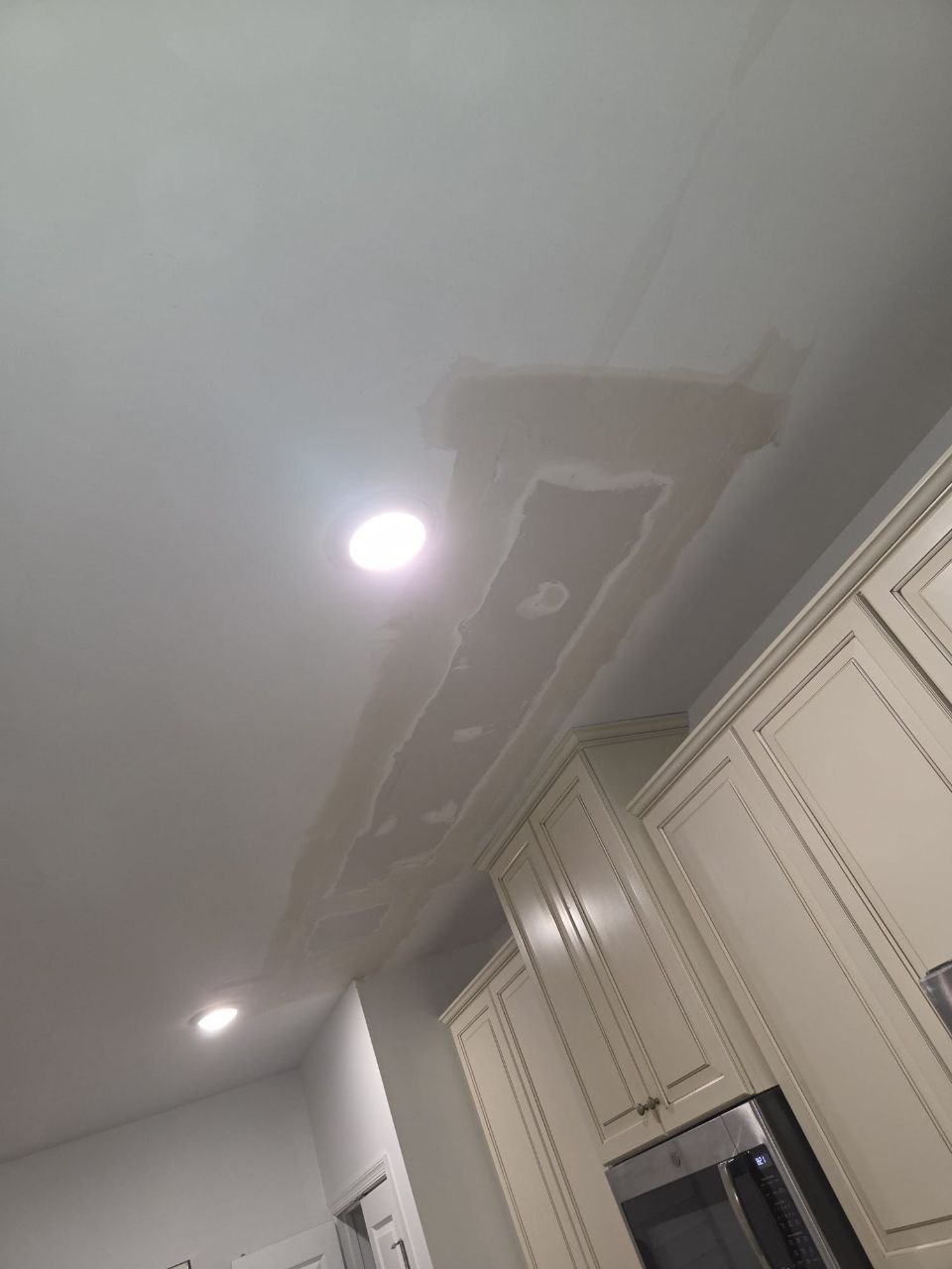 Kitchen ceiling with a fresh drywall patch around recessed lights.