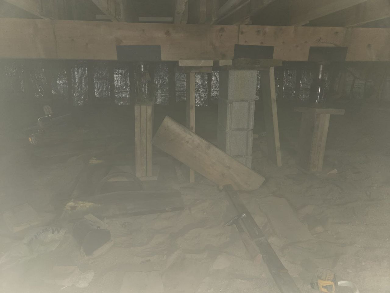 Crawlspace with support jacks, masonry piers, and lumber cribbing.