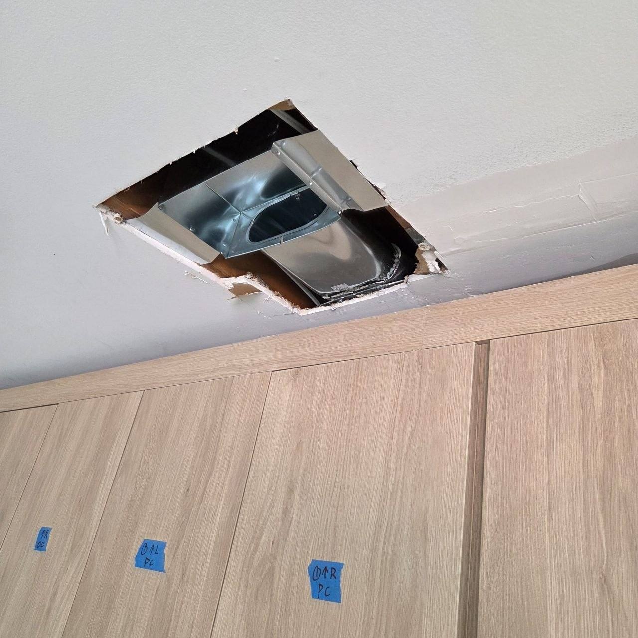 Square cut in a ceiling exposing an HVAC duct above a closet.