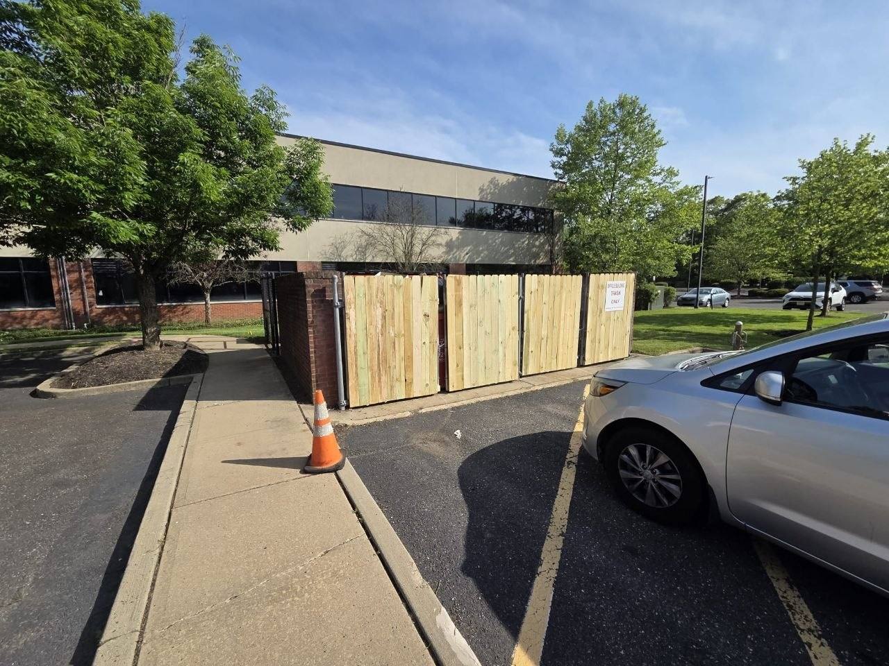 New cedar dumpster enclosure at an office building parking lot.
