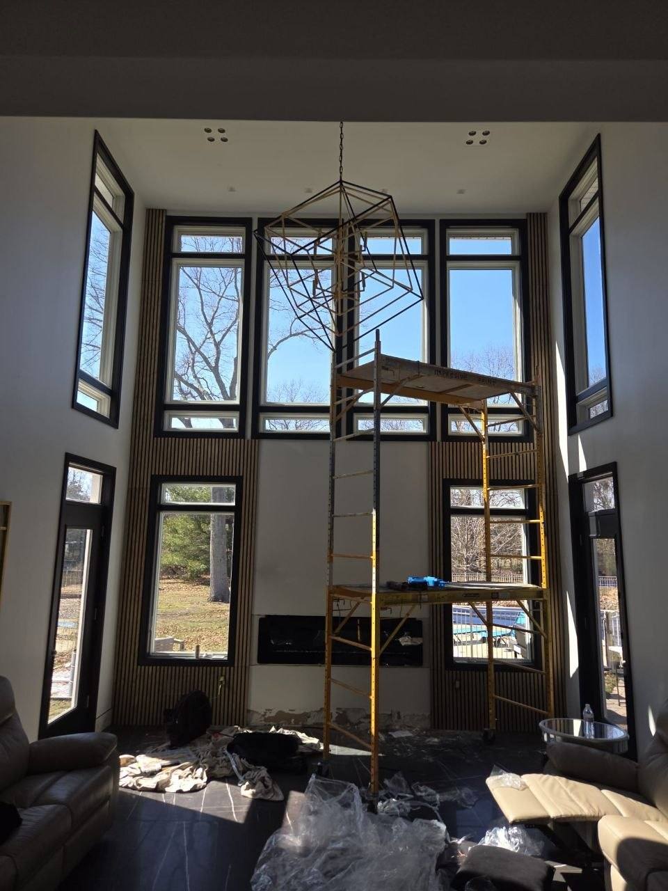 Same room with wood slat walls, a black fireplace, and scaffolding for the chandelier.