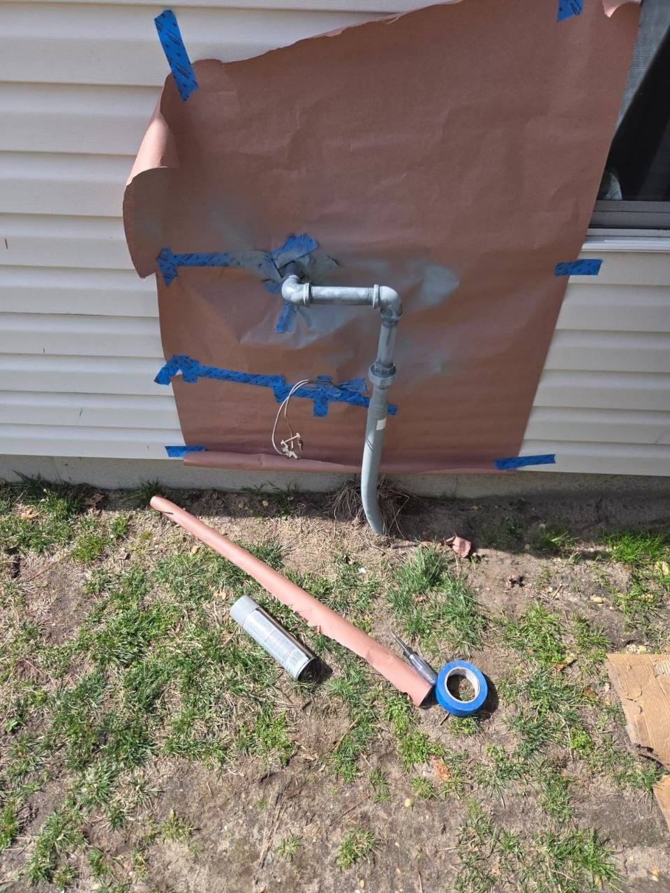 Same pipe primed and painted gray, paper still taped to the siding.