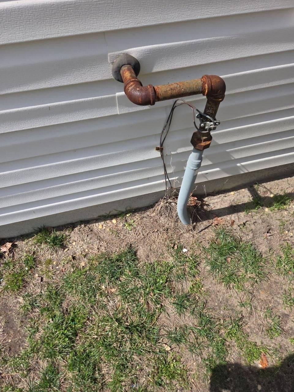 Heavily rusted outdoor water pipe on white vinyl siding.