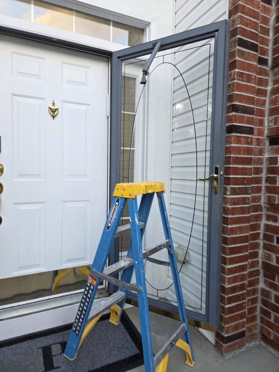 Storm door with a long crack in the glass and a ladder on the stoop.