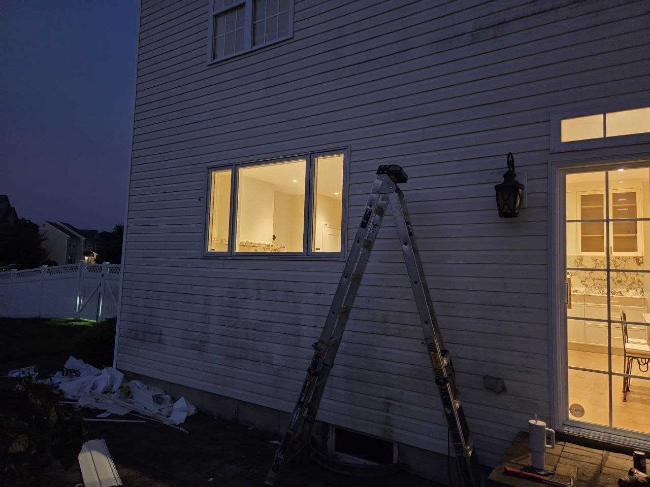 Dusk exterior with a ladder against the house and new windows glowing.